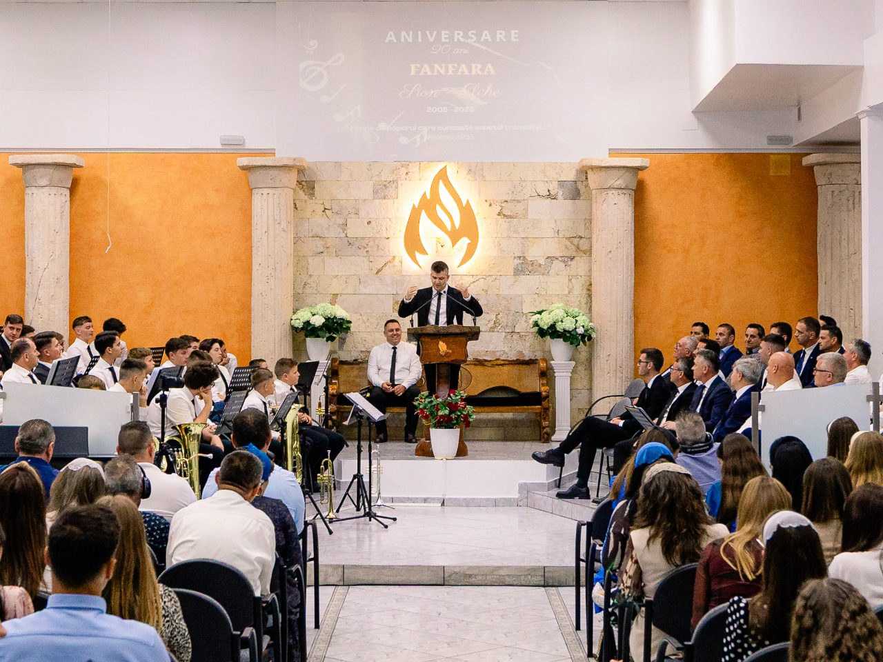 Congregația bisericii la un serviciu de închinare, văzută din spatele sălii, cu amvonul în față.